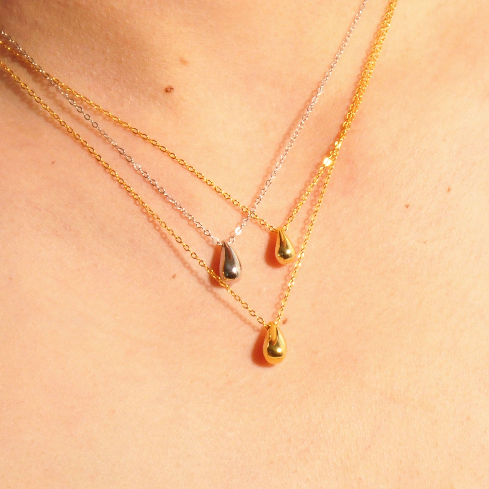 Modell trägt zwei goldene und eine weißgoldene Aqua Halskette mit Wassertropfen-Anhängern, minimalistisches Design, 925er Silber vergoldet.