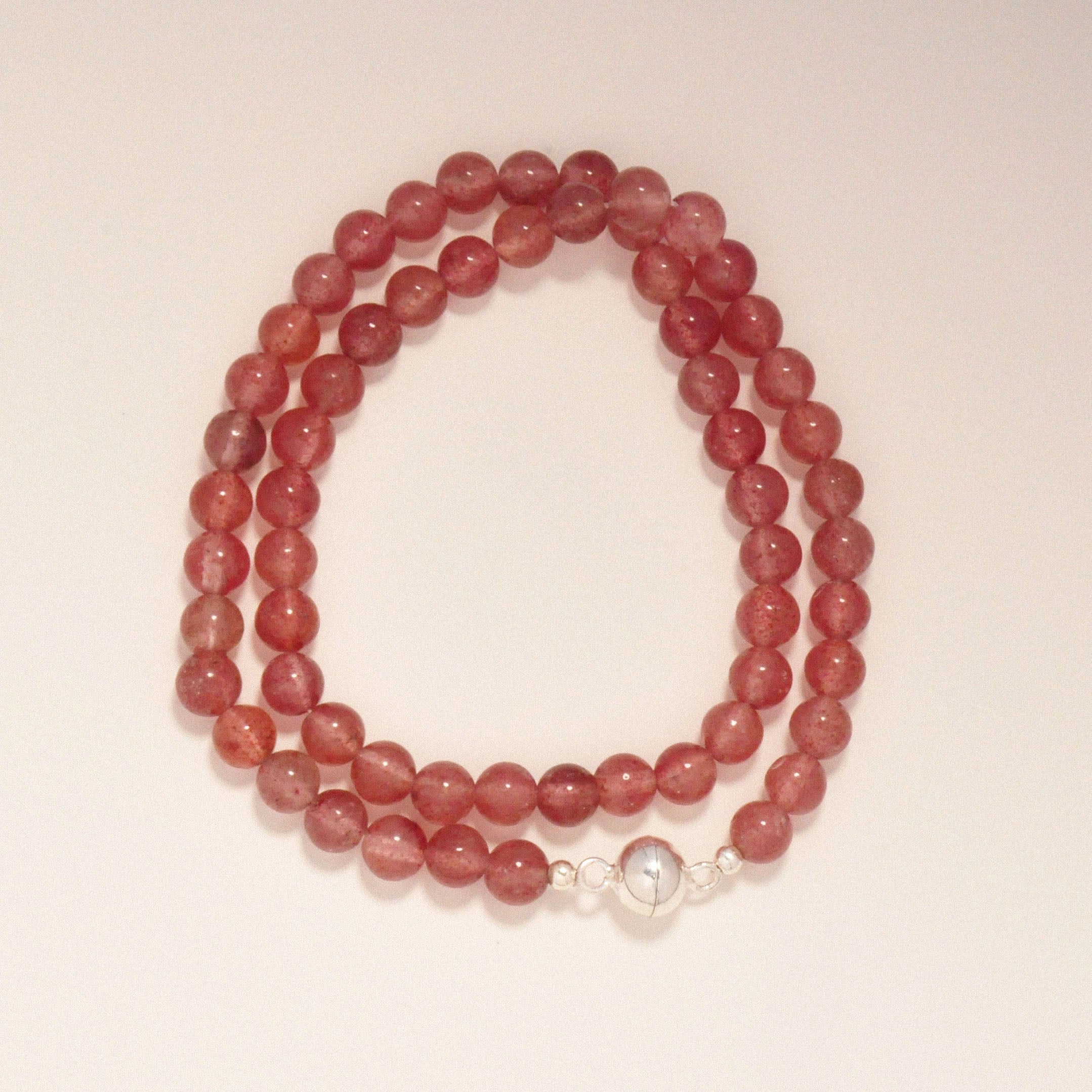 Erdbeerquarz Berry Bliss Halskette auf einer weißen Oberfläche.