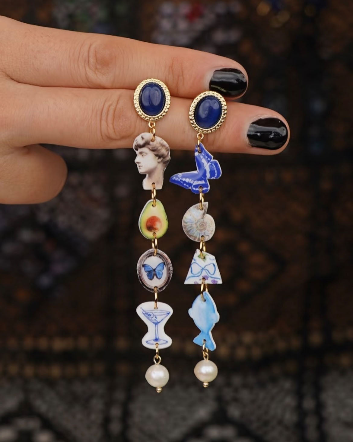 Hand hält die Playful Drops Ohrringe mit Avocado-, Schmetterlings- und Skulpturmotiven – Luumi Creative Hamburg.